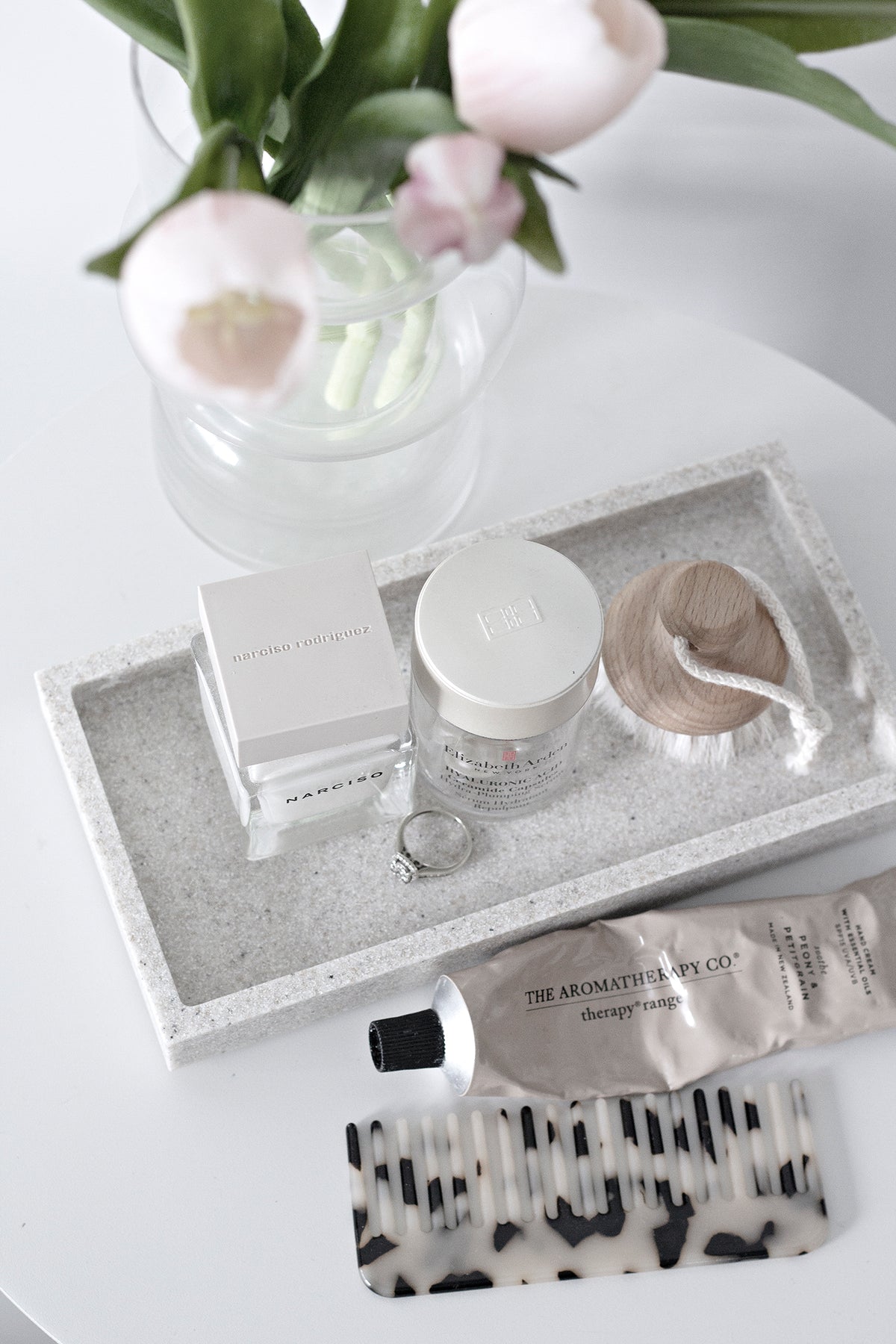 Black and white acetate comb on a white tray with a glass vase of tulips and a candle
