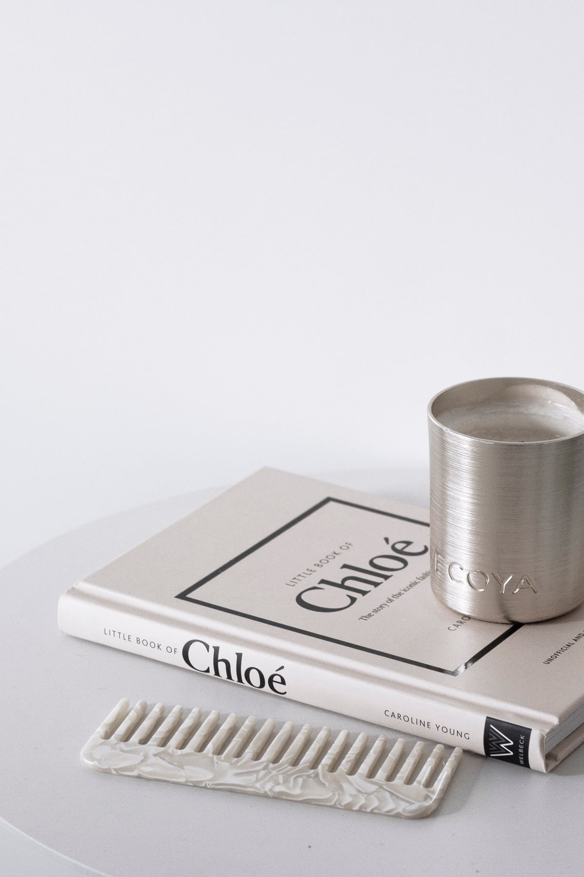 Cream acetate comb beside stacked books and a brushed silver tumbler