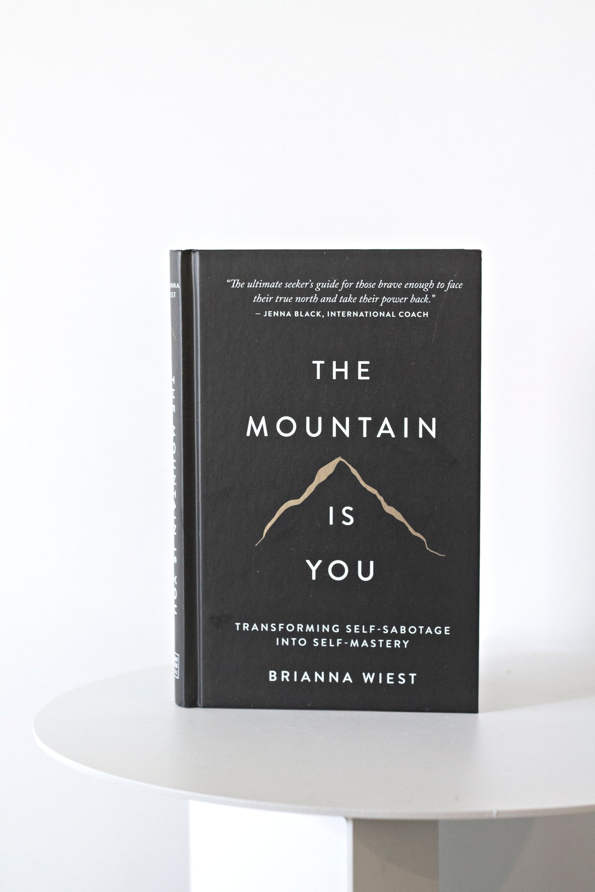The Mountain Is You hardcover standing alone on a round white pedestal table in soft daylight