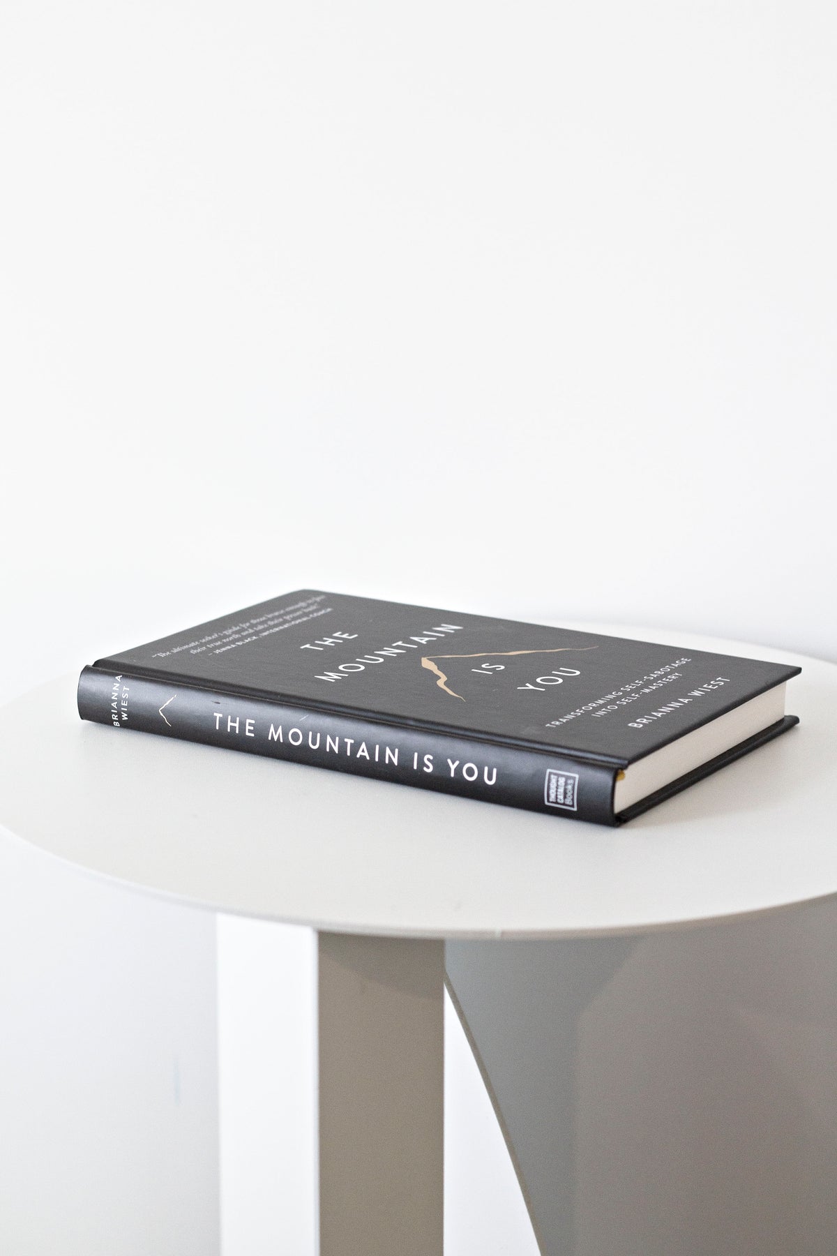 The Mountain Is You by Brianna Wiest lying flat on a round white table with the spine facing forward