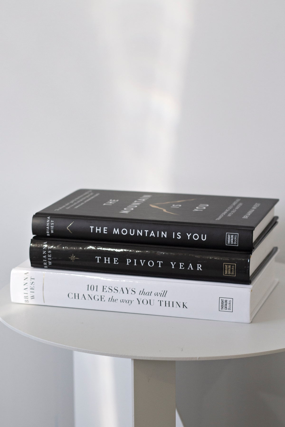 Three Brianna Wiest hardcovers stacked flat on a round white table with The Mountain Is You on top