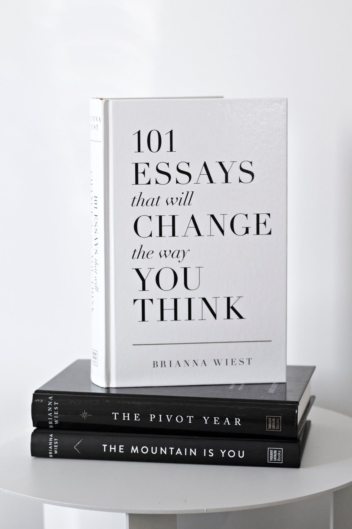 The 101 Essays paperback standing upright on a stack of two hardcovers on a round white table