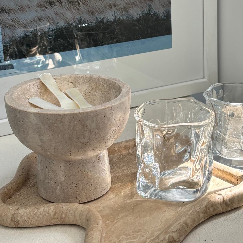 Mother of pearl spoon in a stone mortar beside glass tumblers on a timber board