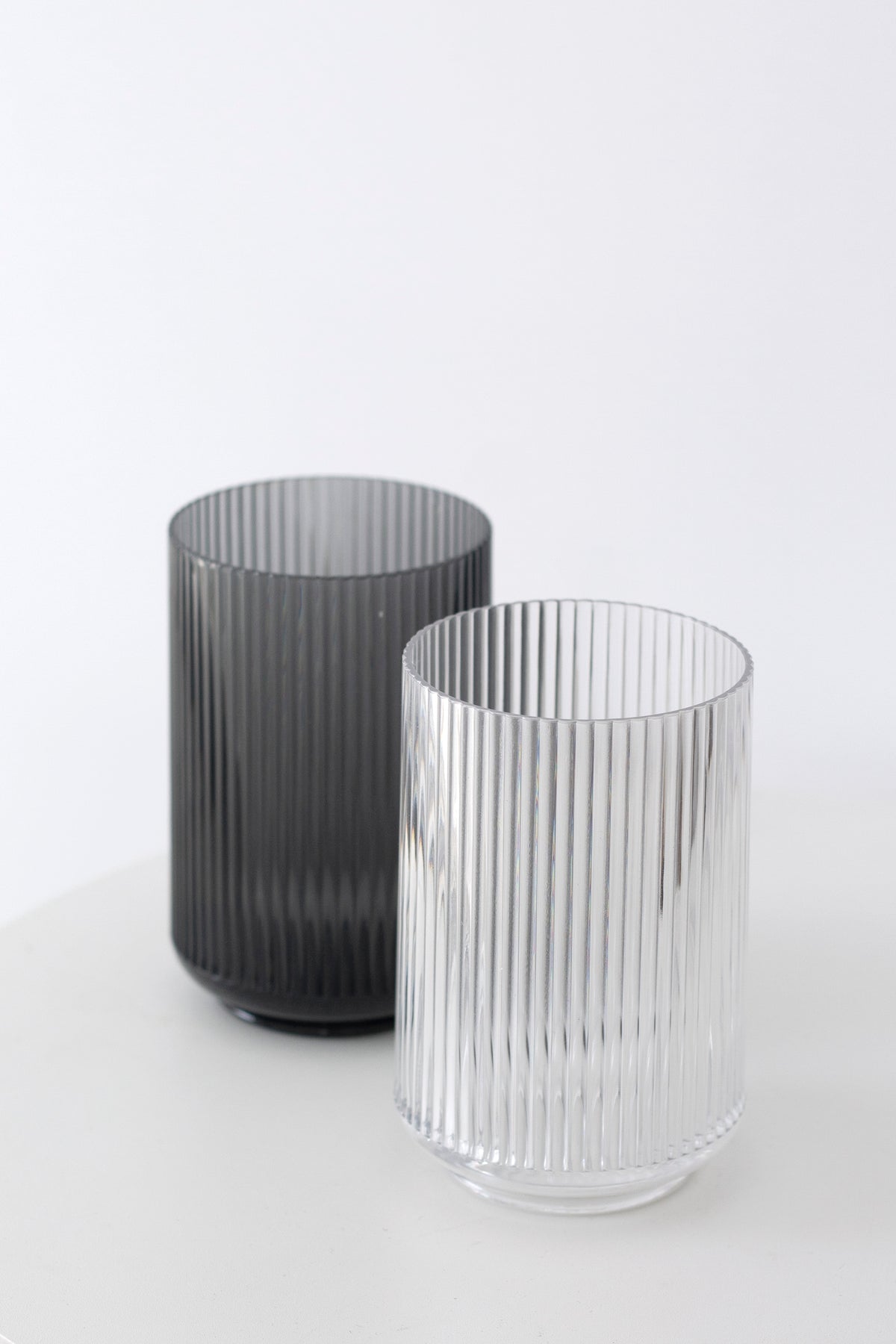 Smoke and clear fluted tumblers standing side by side on a white surface