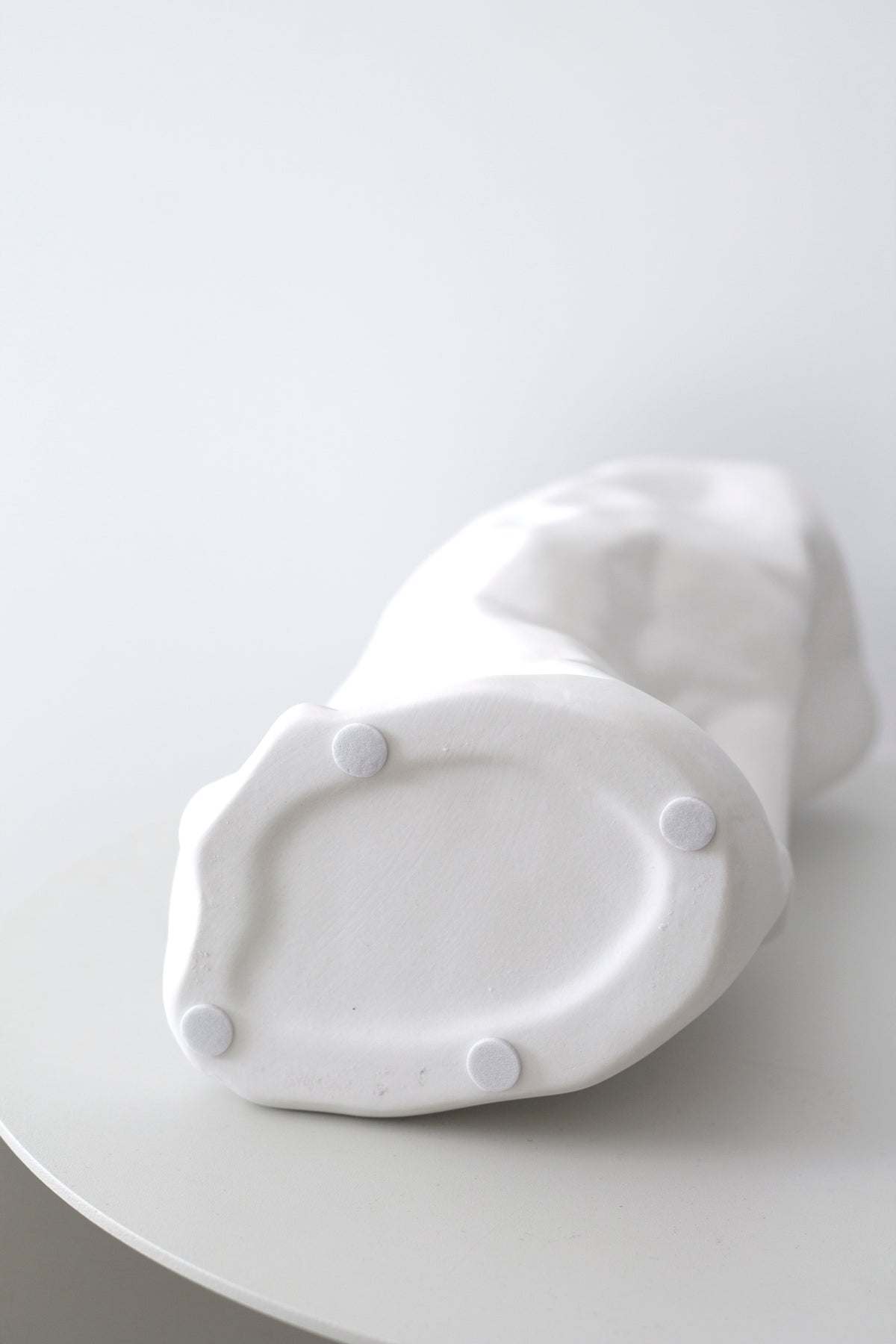 White crumpled vase lying on its side on a round table, showing the creased body
