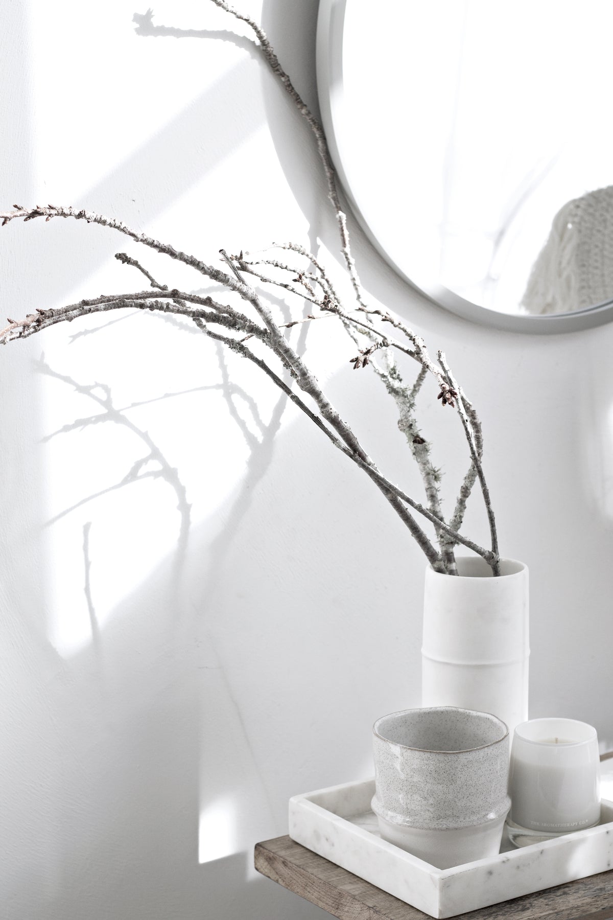 Umbra Hub round grey mirror beside bare branches in a vase
