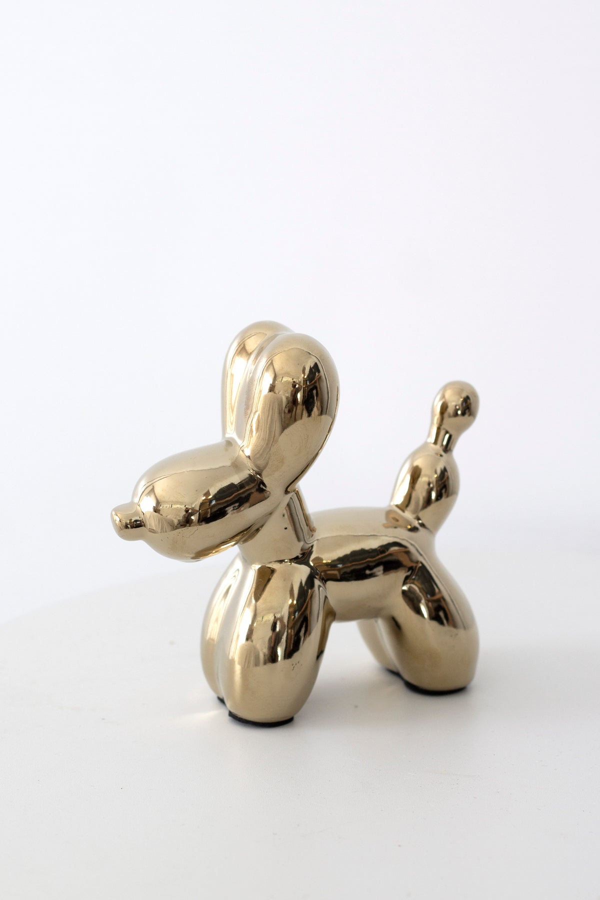 Gold ceramic balloon dog sculpture, side view on a white background