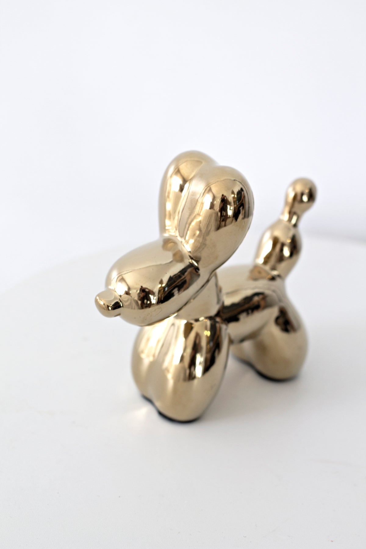 Gold ceramic balloon dog sculpture on a white surface, angled view