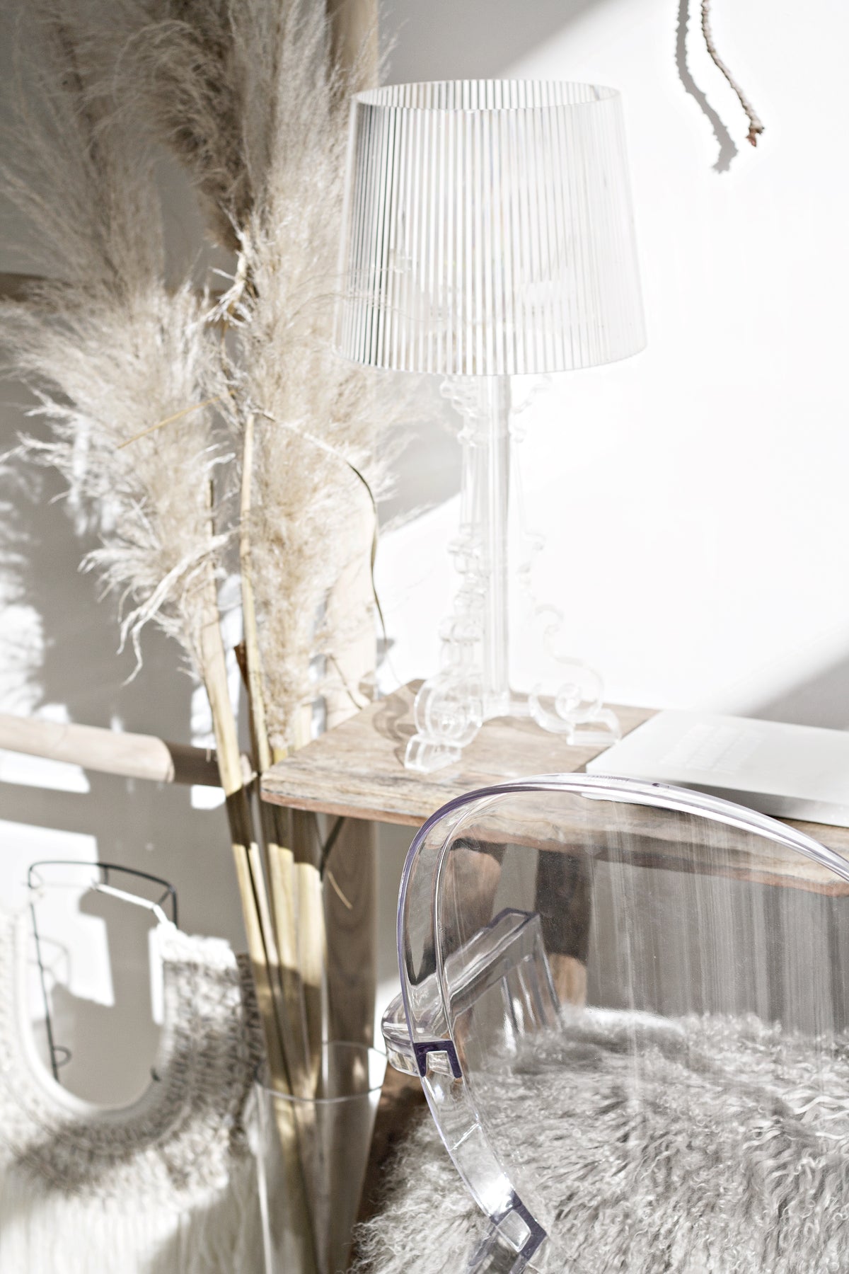 Clear acrylic chair with a sheepskin beside a ribbed lamp and pampas grass