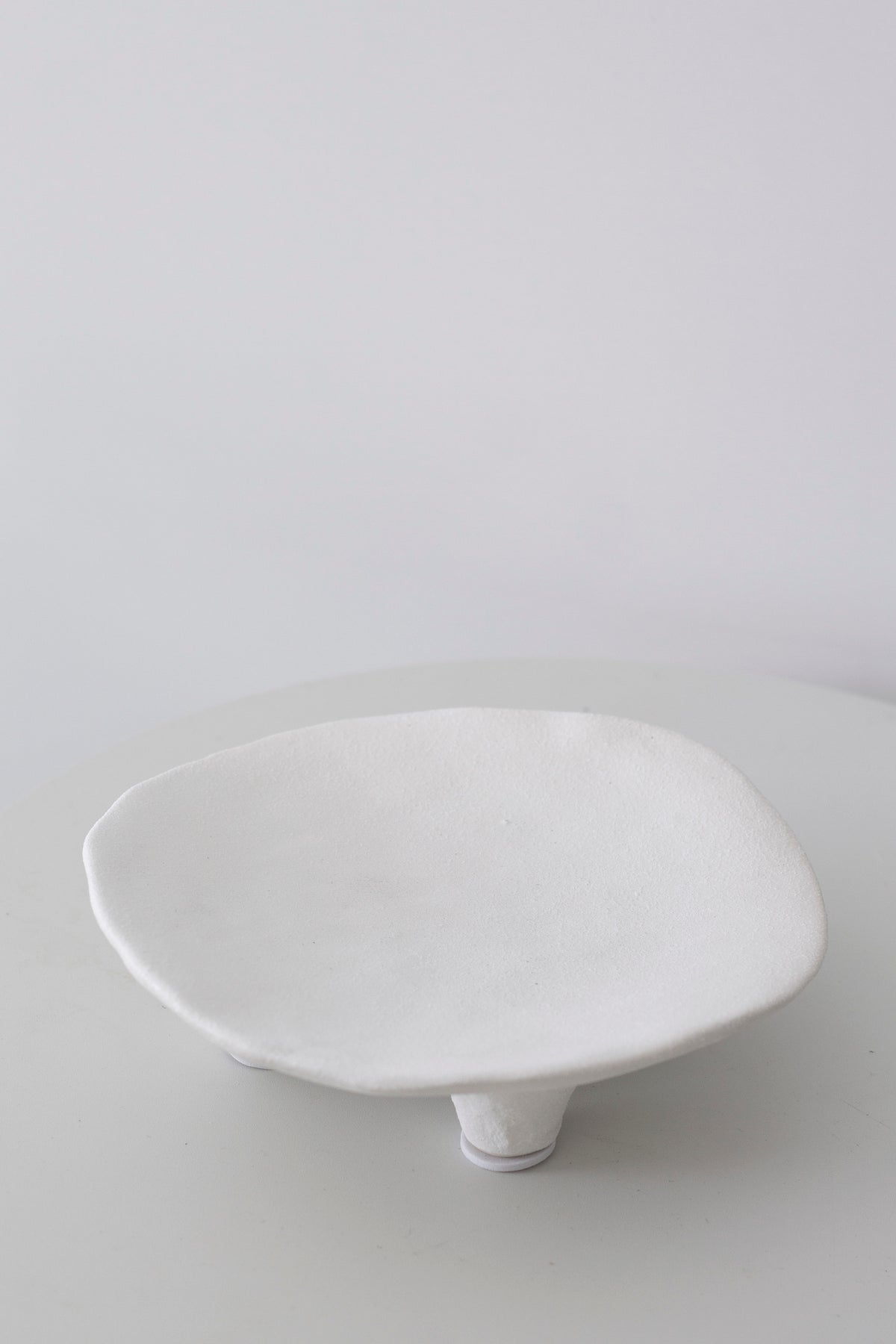 White ceramic dish seen side on, the shallow bowl lifted clear of the surface
