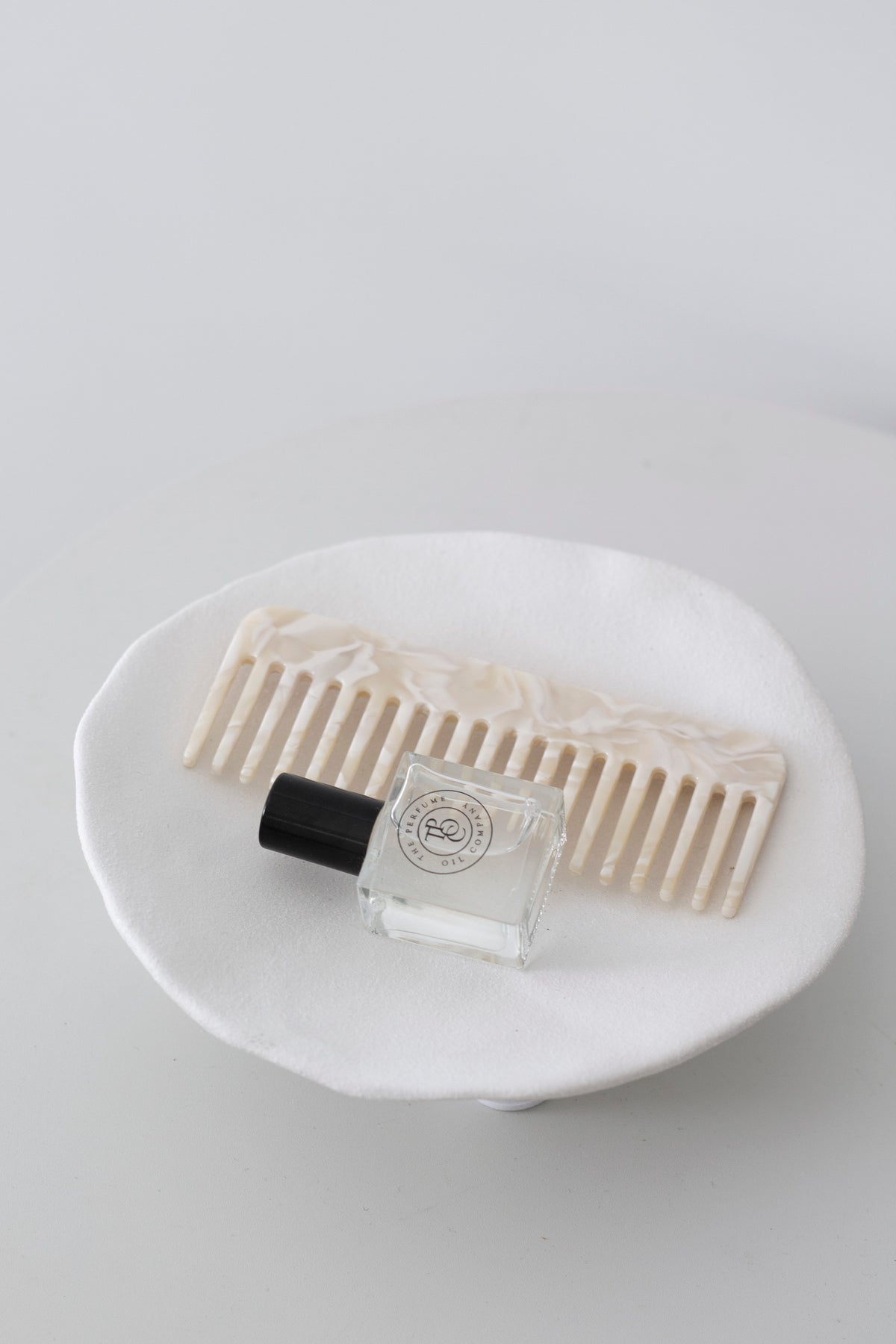 Comb and a small perfume bottle resting in the white ceramic dish