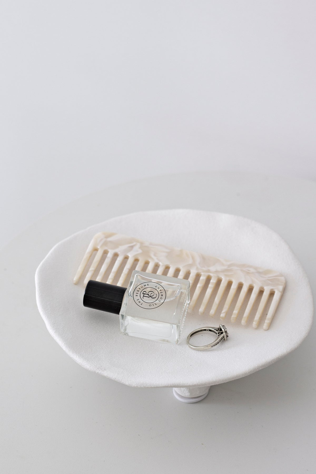 Cream acetate comb on a white pedestal dish with a perfume bottle and a ring
