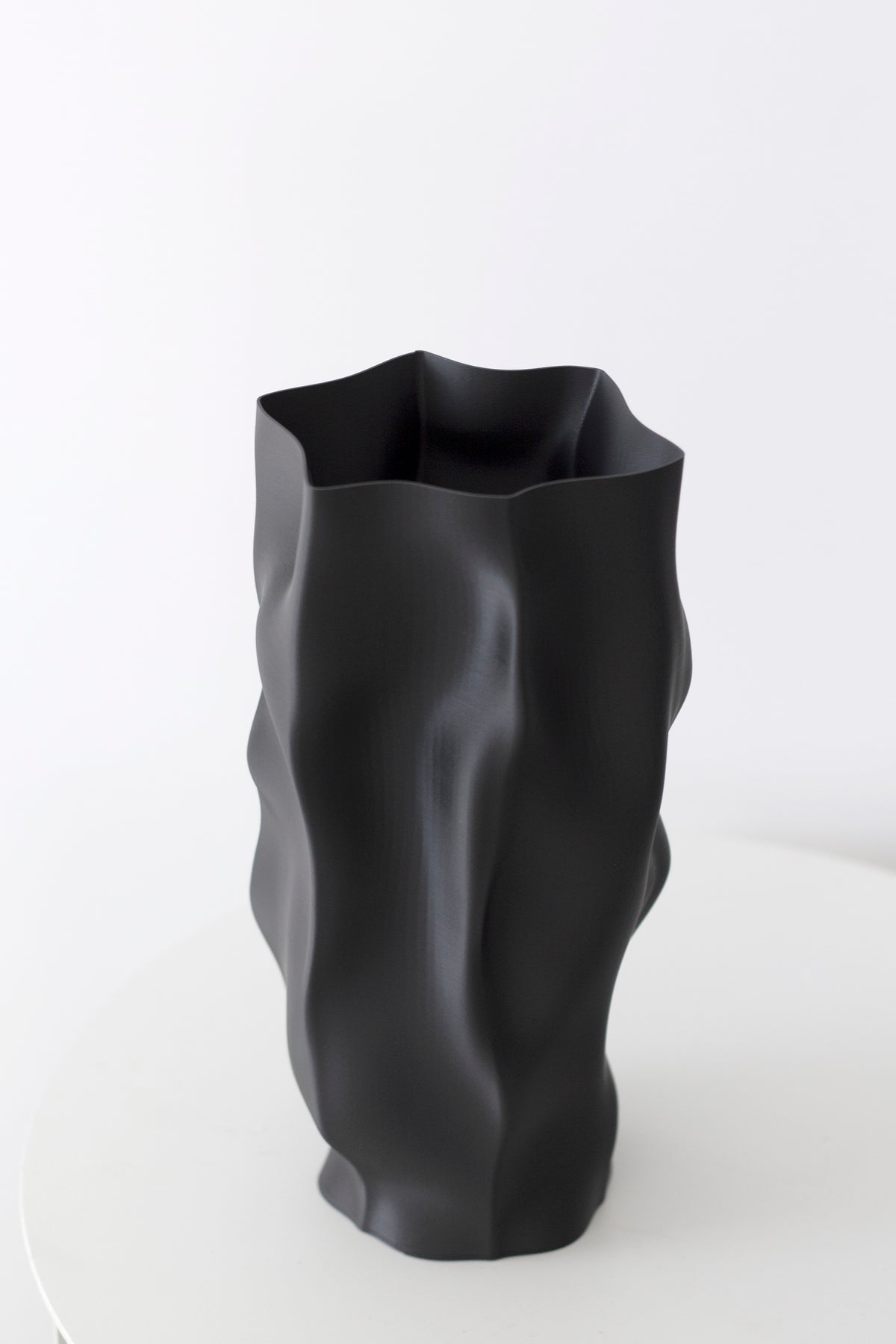 Matte black ripple vase turned to show the uneven rim and deep vertical folds