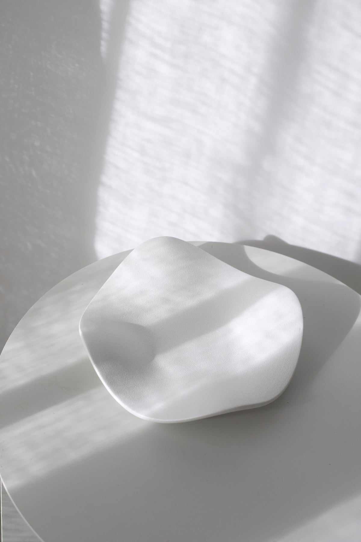 Matte white wave tray viewed from above on a white table with dappled light across the surface