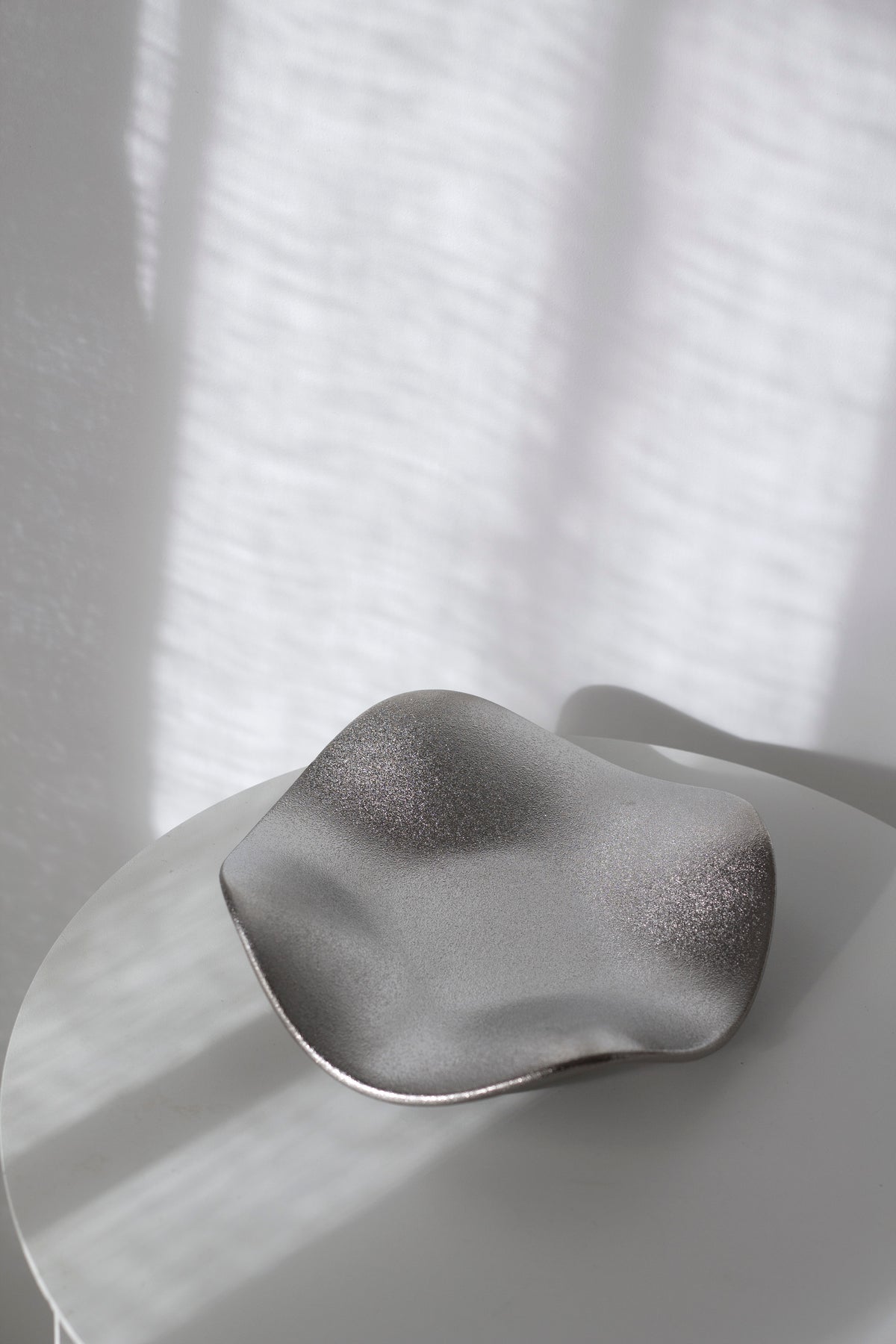 Silver wave tray seen from above on a white table, soft shadows falling across the sparkling finish