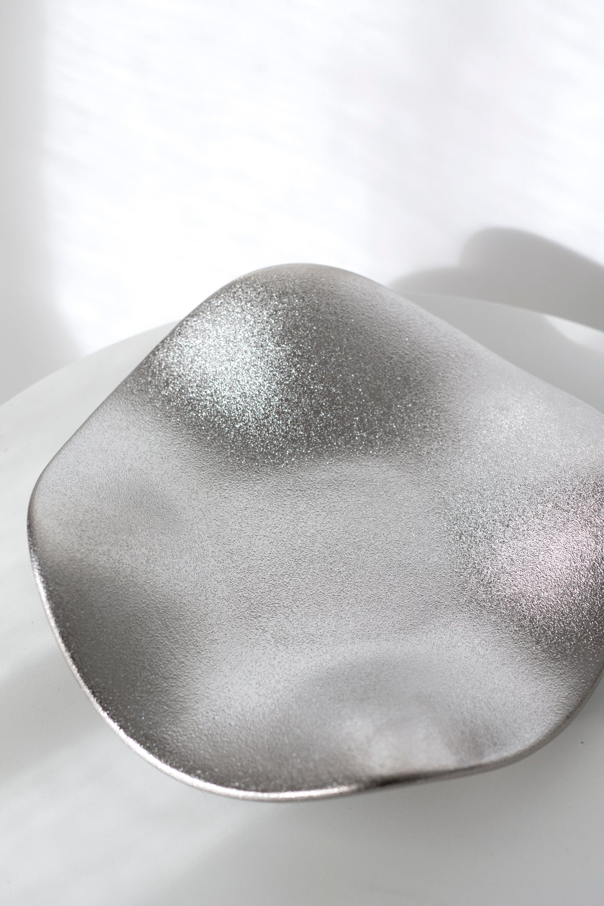 Close view of the silver wave tray, the speckled metallic glaze catching the light across the ripples