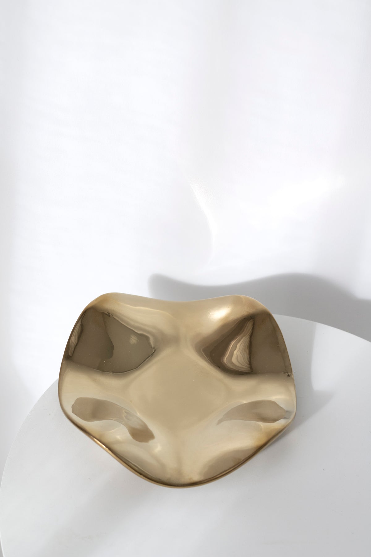 Polished gold wave tray catching the light on a white round table, its mirrored surface reflecting the room