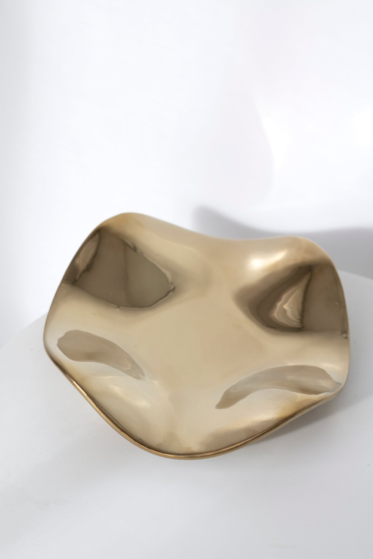 Polished gold wave tray at a three-quarter angle, reflections pooling in the hollows of the form