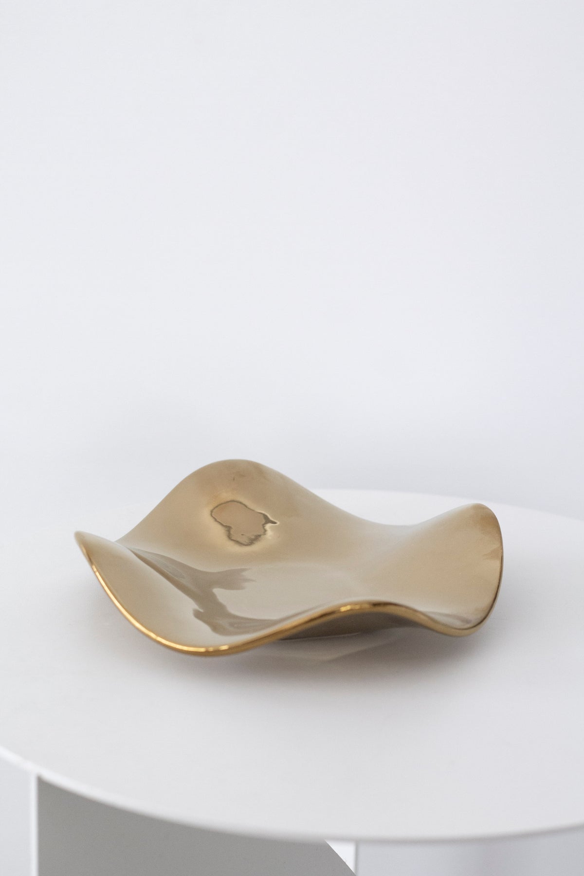 Pale gold wave tray on a white round table, its glossy surface catching a soft highlight