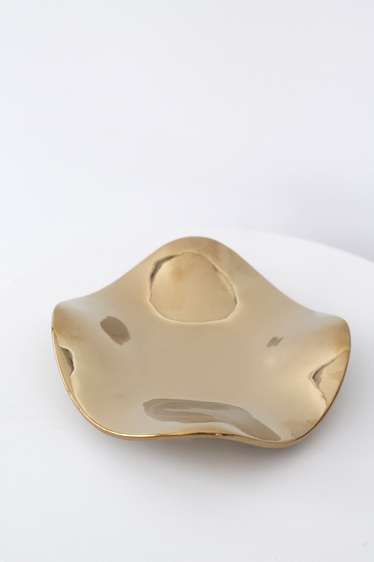 Polished gold wave tray from above, the mirrored finish rippling across the curved surface