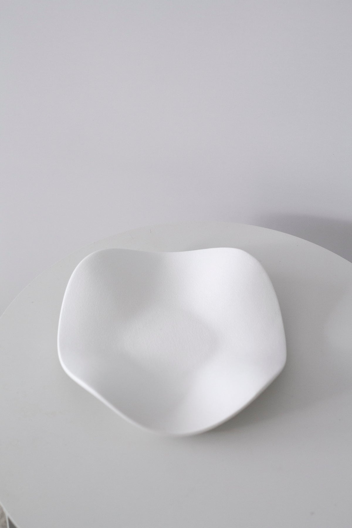 Matte white wave tray from above on a white table, the soft undulating edge in full view