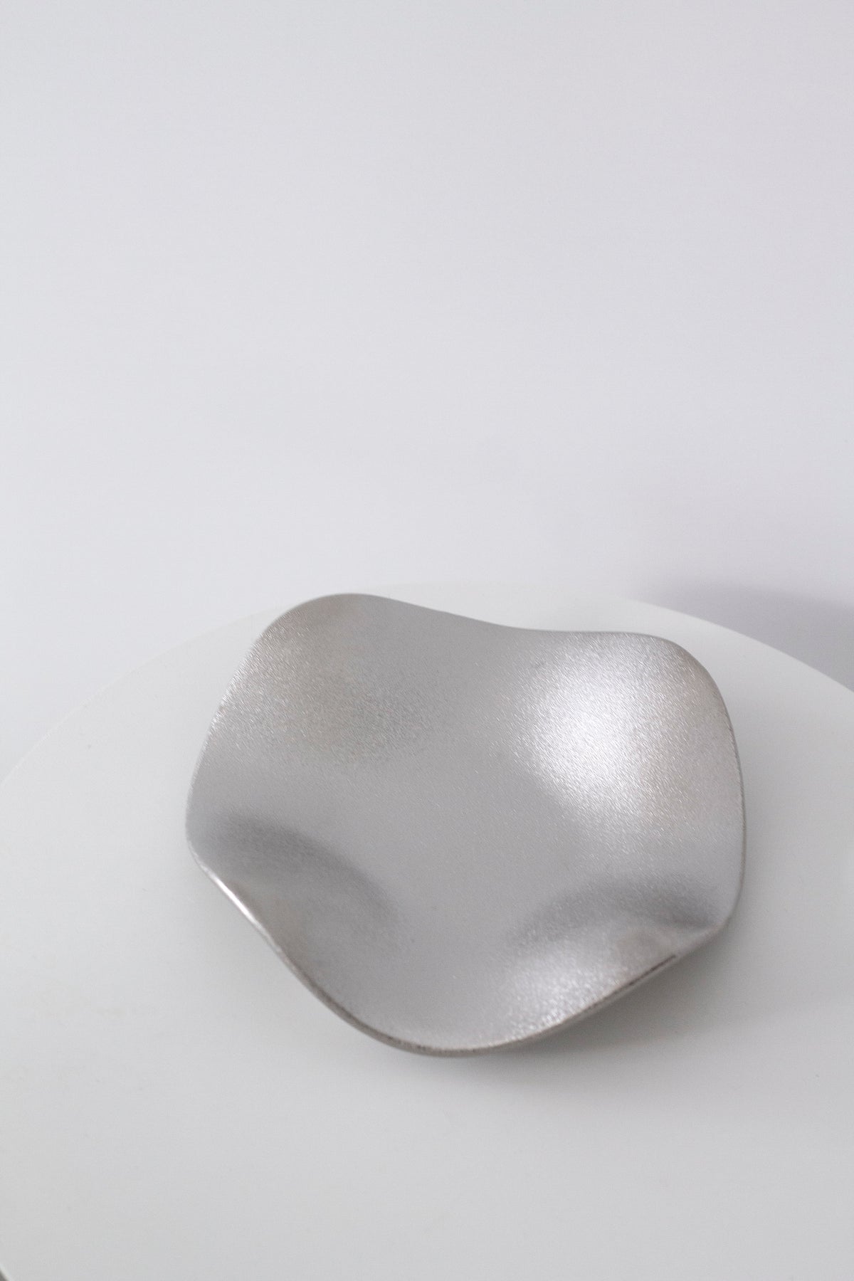 Silver wave tray from above on a white table, the pale metallic finish softly lit