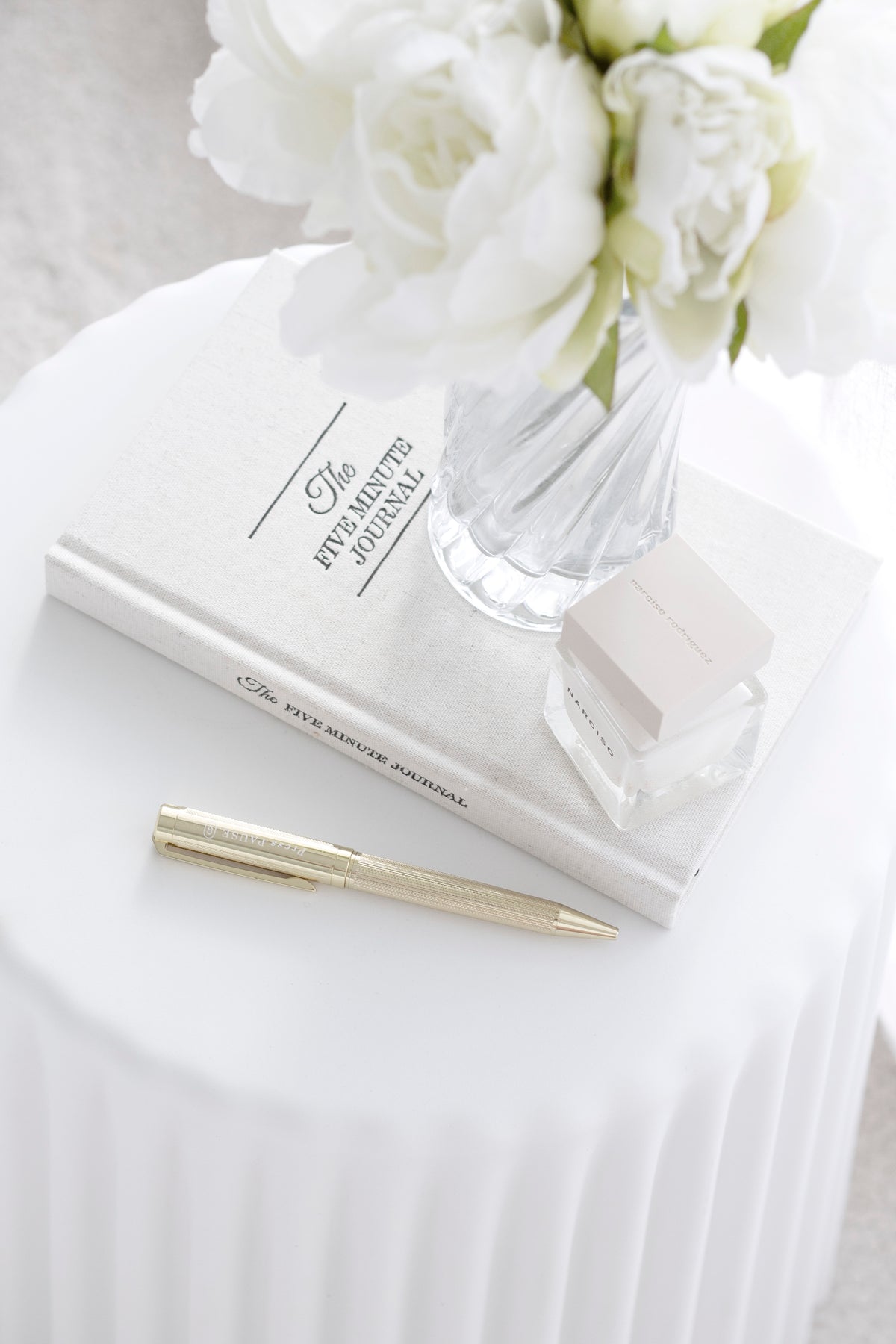 Looking down on a white ribbed stool with a glass vase of white peonies, a journal and a pen