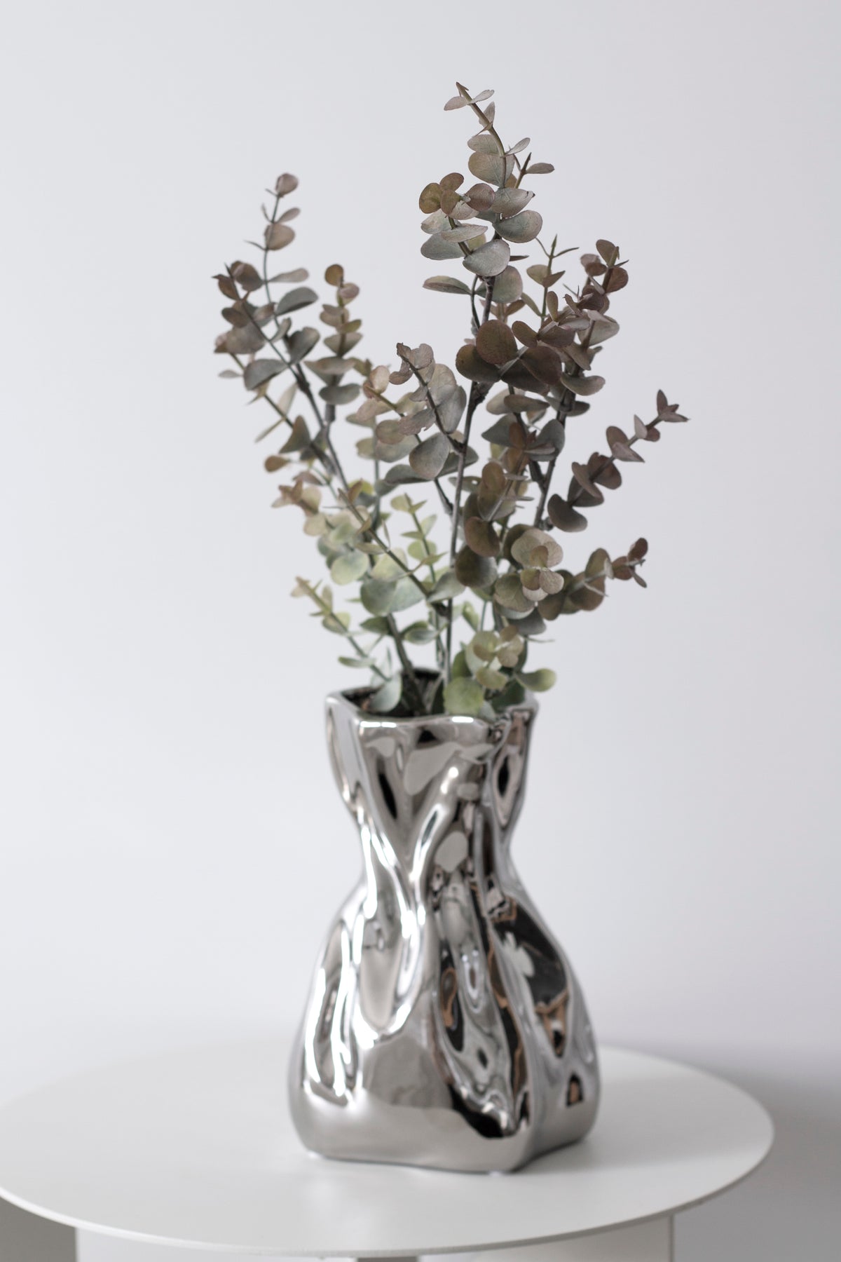 Faux eucalyptus stems in a sculptural swirl vase