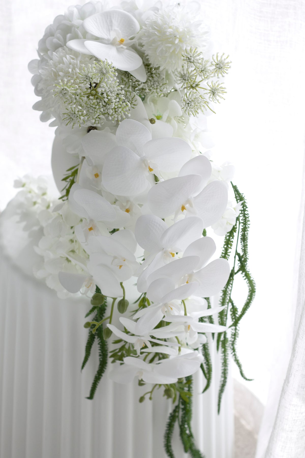 Close crop of the bouquet against sheer curtains, orchid blooms layered over hydrangea