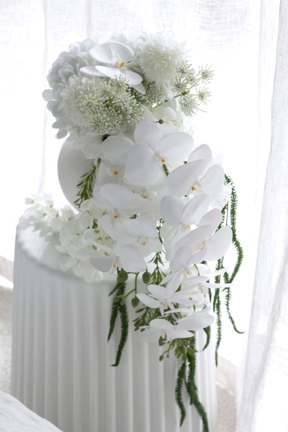 The arrangement by a window, sheer curtain diffusing light across the white blooms