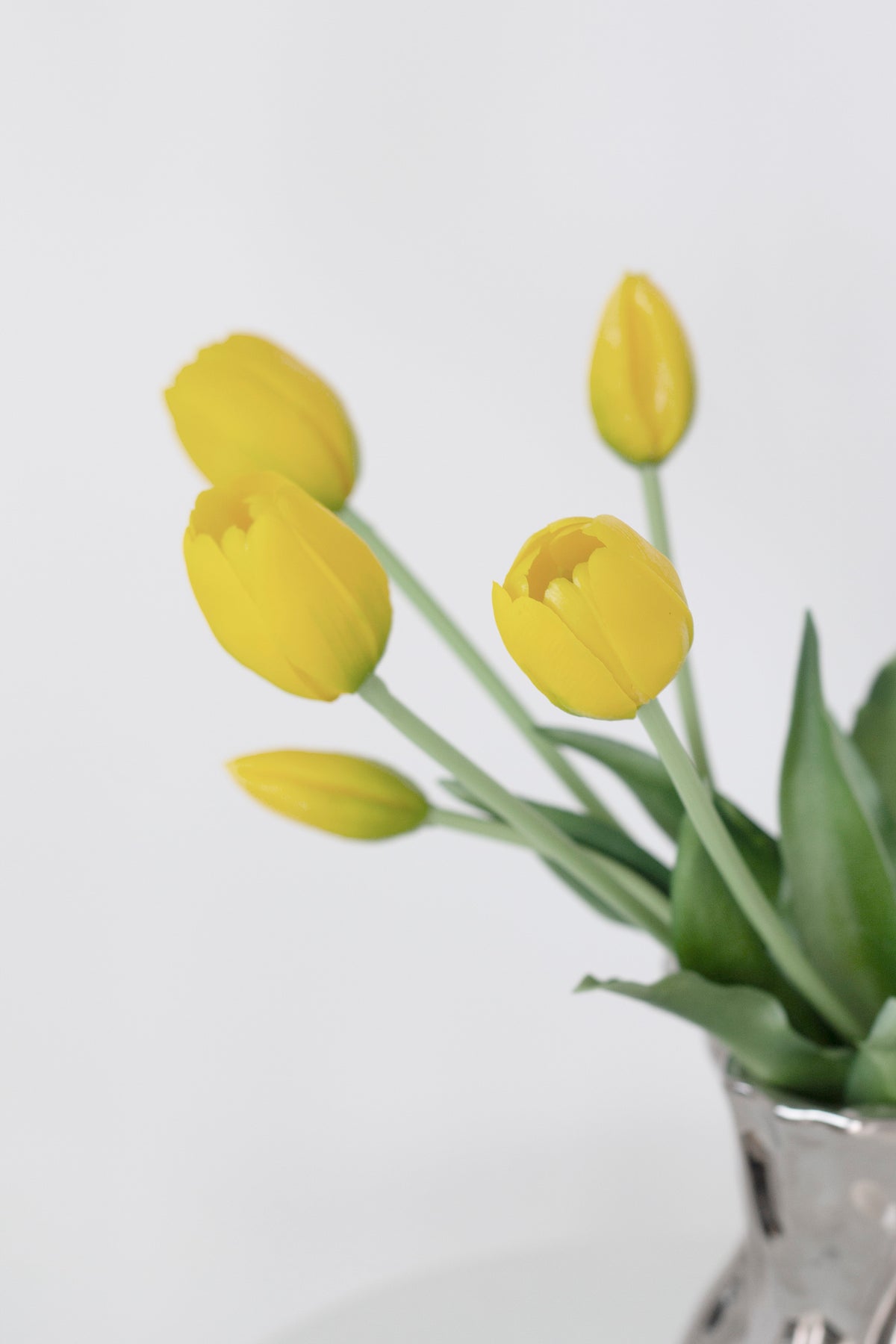 Yellow faux tulips in a vase against a pale grey wall