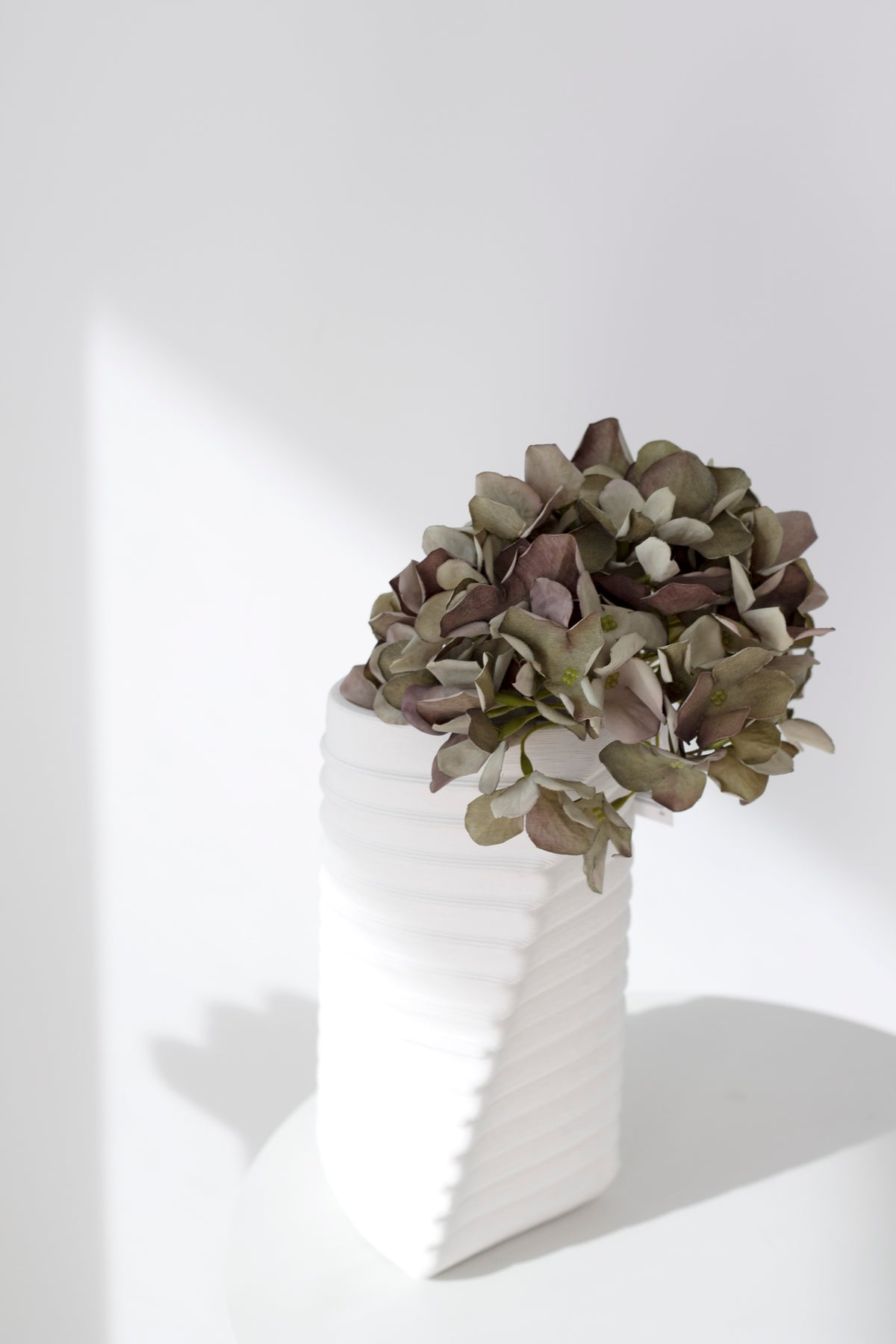 Green faux hydrangea in a white angular vase on a white shelf