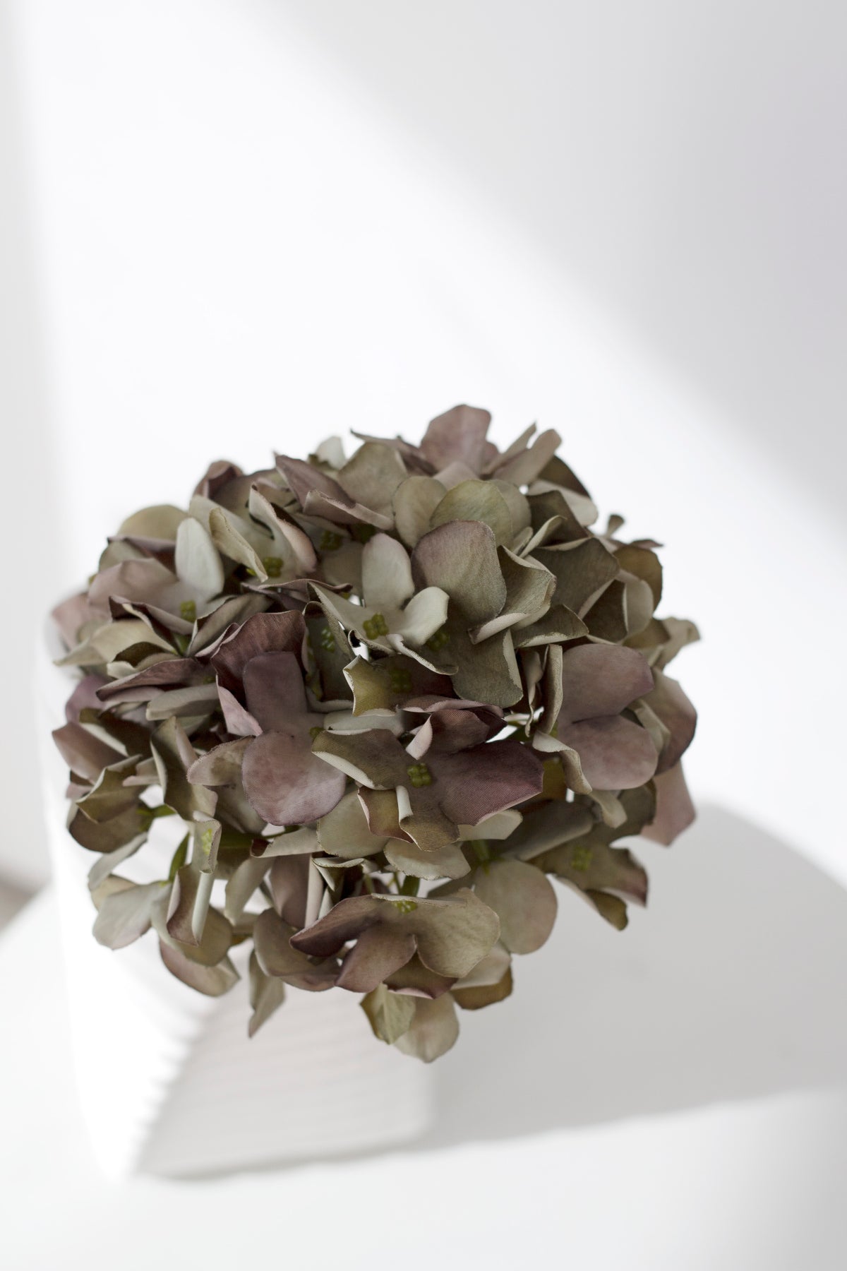 Close view of the green faux hydrangea head in a white vase