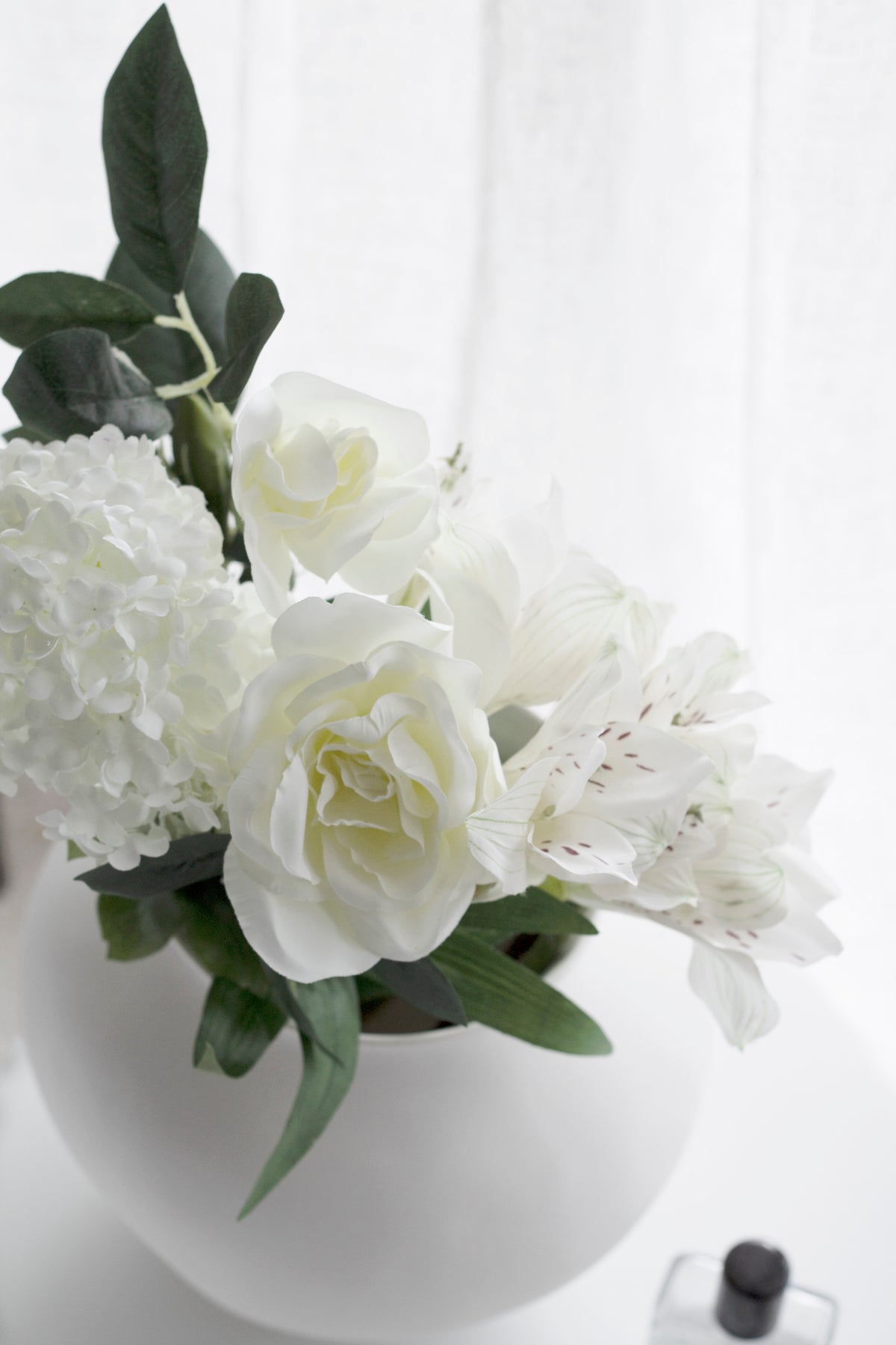 Gardenia, hydrangea and blossom arranged together in a round white vase