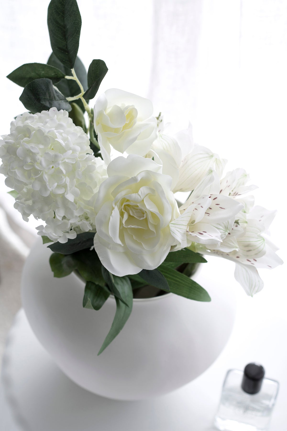 White gardenia, hydrangea and blossom massed in a round white vase