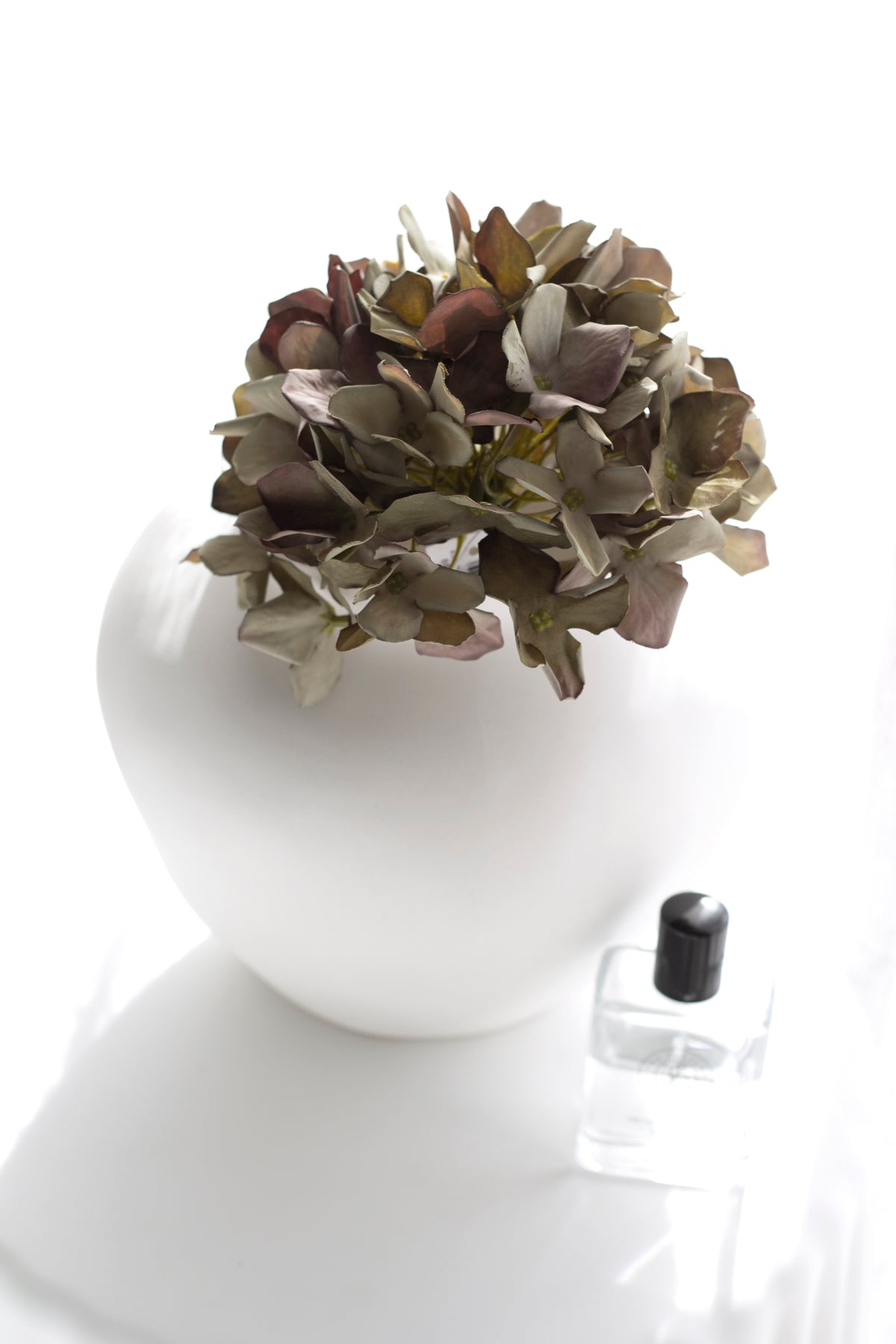 Green faux hydrangea in a round white vase on a white plinth