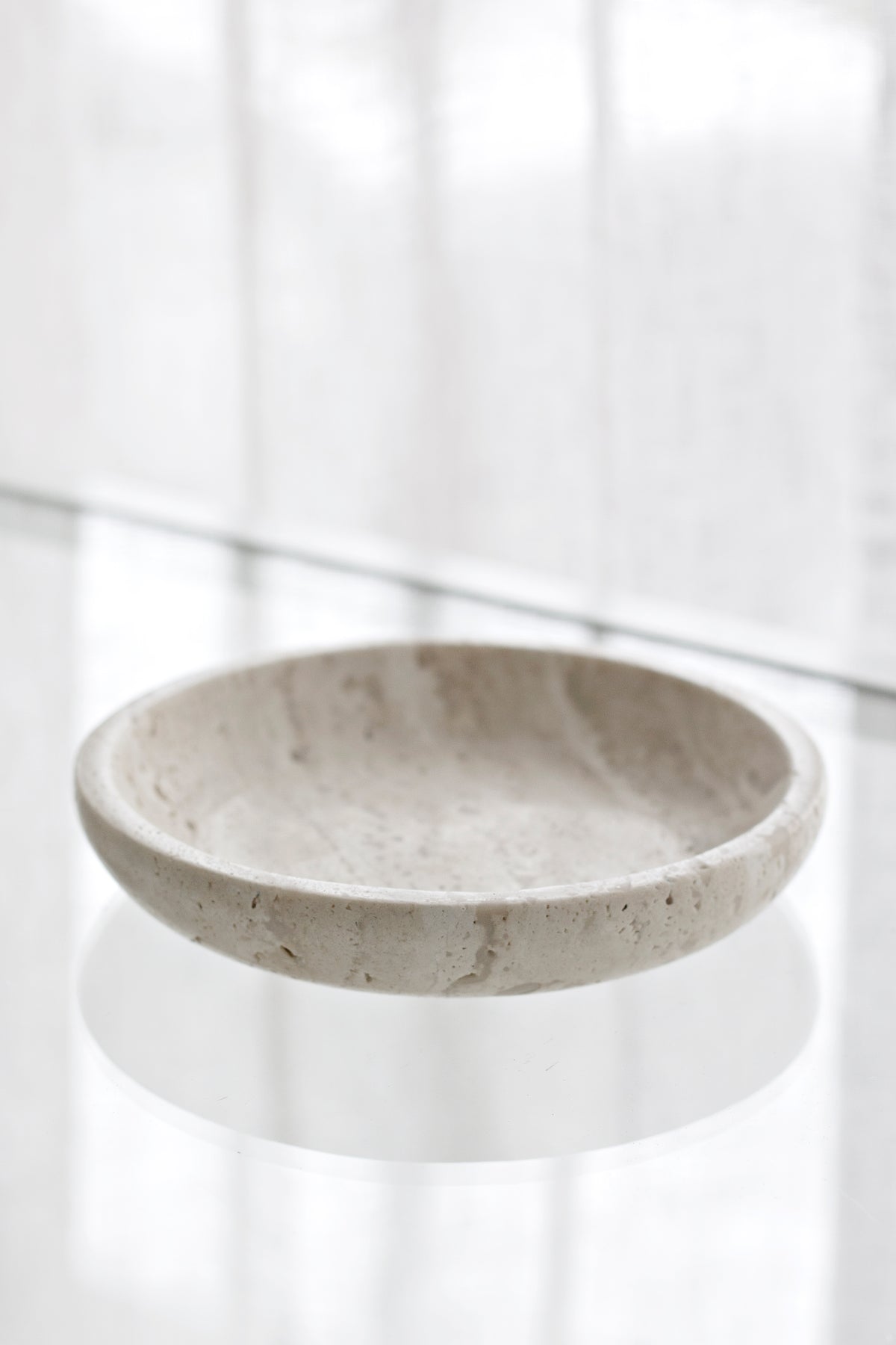 Travertine tray photographed low on a white surface with a curtain behind