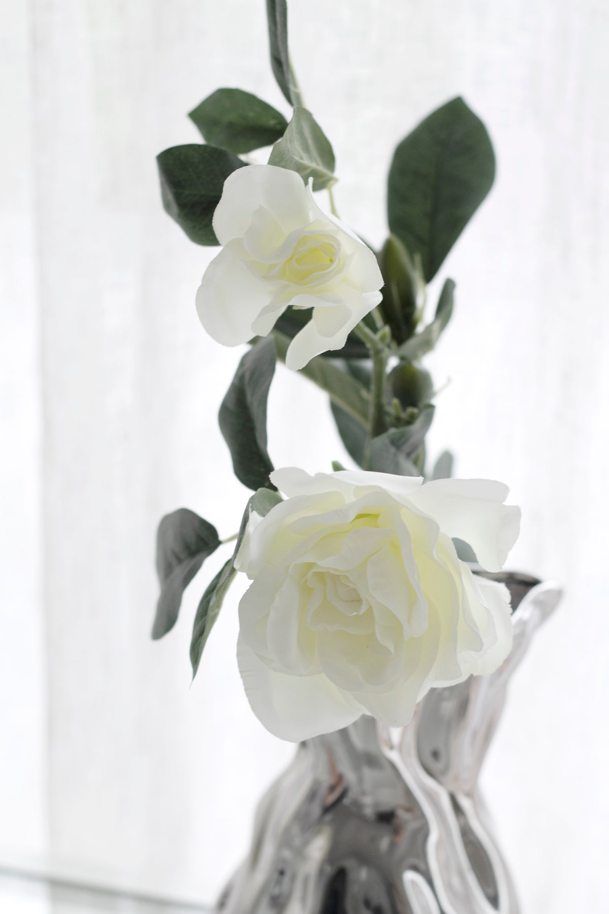 White gardenia blooms in a mercury glass vase against a sheer curtain