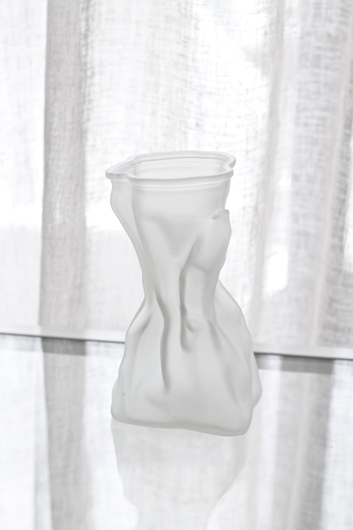 Frosted crinkle vase standing on a glossy dark surface with a sheer curtain behind
