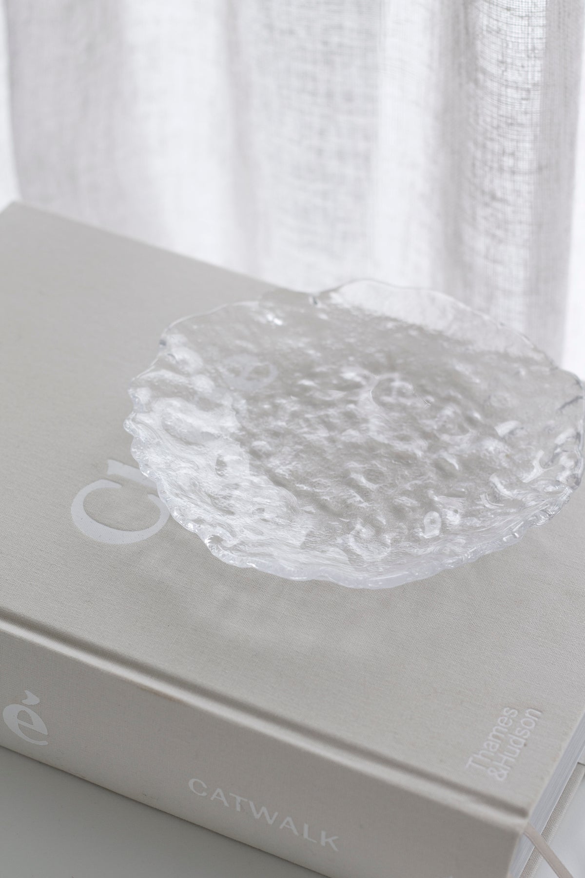 Glacier glass tray resting on a stack of books against a sheer curtain