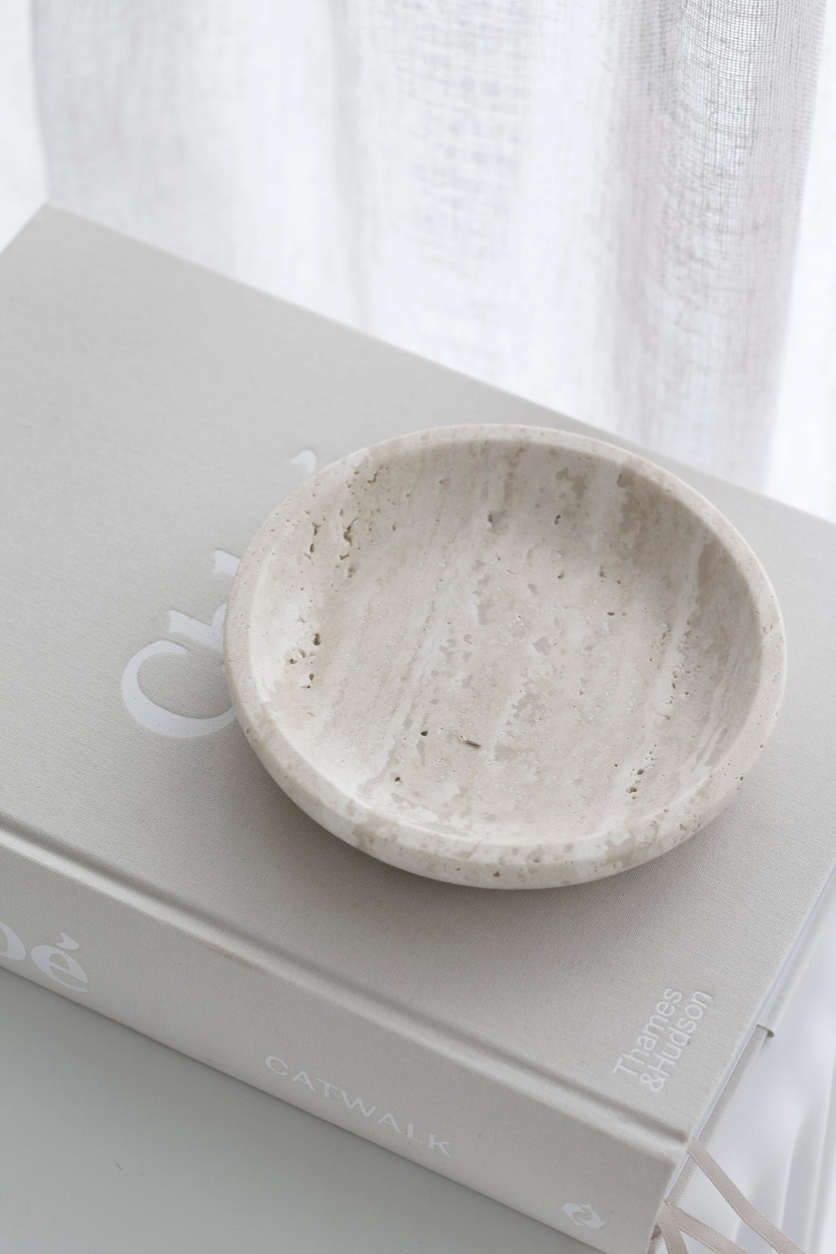 Tray resting on a book beside a small white cup, linen curtain behind