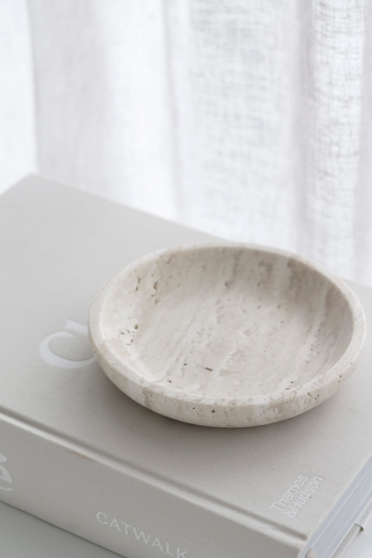 Travertine tray on a large format book with a linen curtain filling the background
