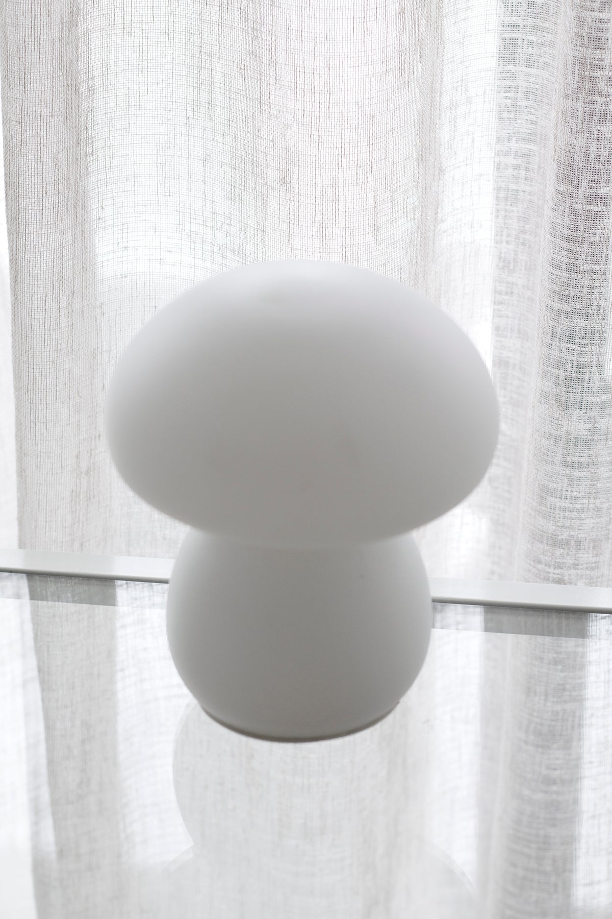 White mushroom lamp on a sill in front of a sheer linen curtain