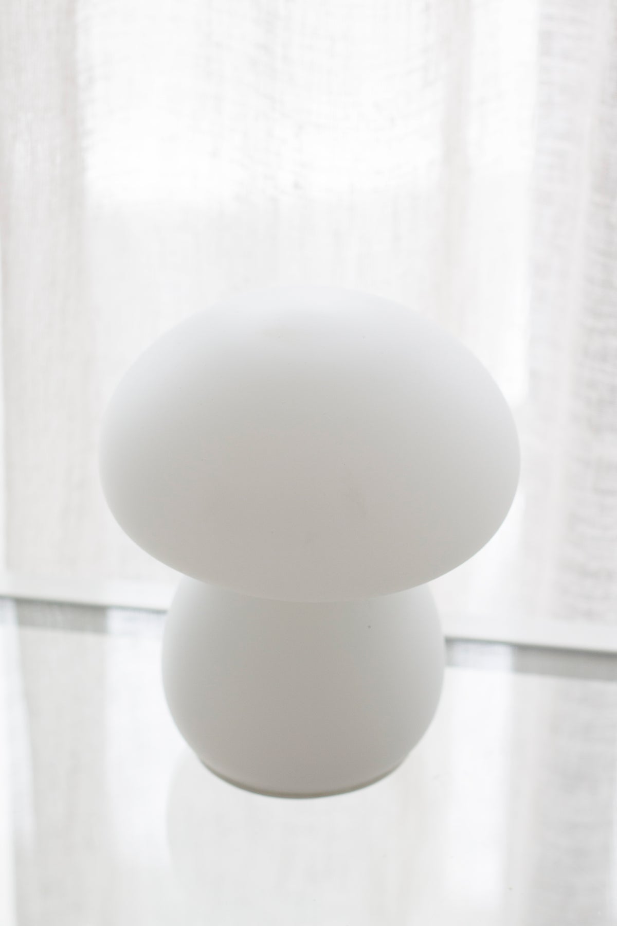 Mushroom lamp seen straight on against soft daylight through linen