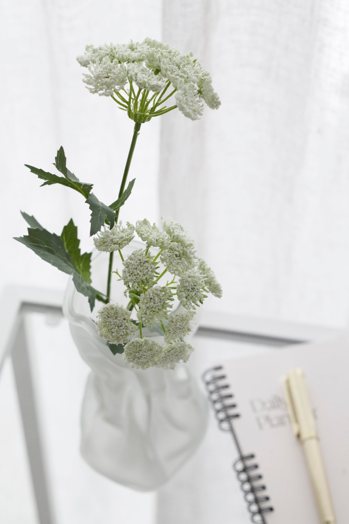 Queen Anne's Lace faux stem in a frosted twisted vase on a glass table beside a notebook and pen