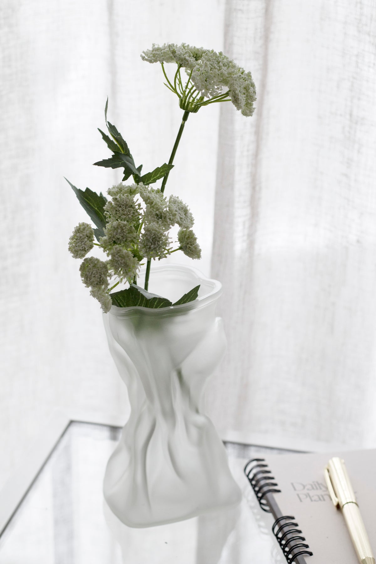 Queen Anne's Lace faux stem in a frosted vase on a glass table with a notebook and gold pen