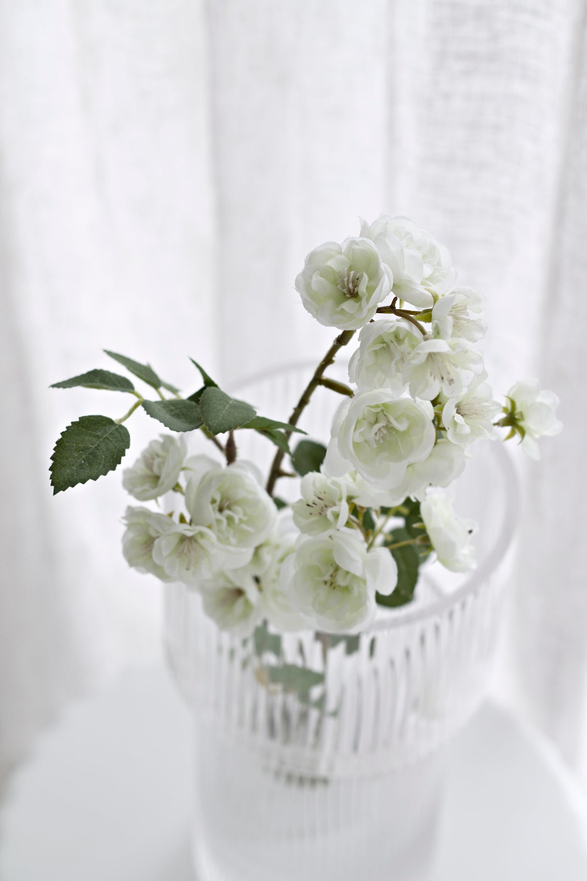 Cream faux rambling roses and buds spilling over the rim of a clear glass vase
