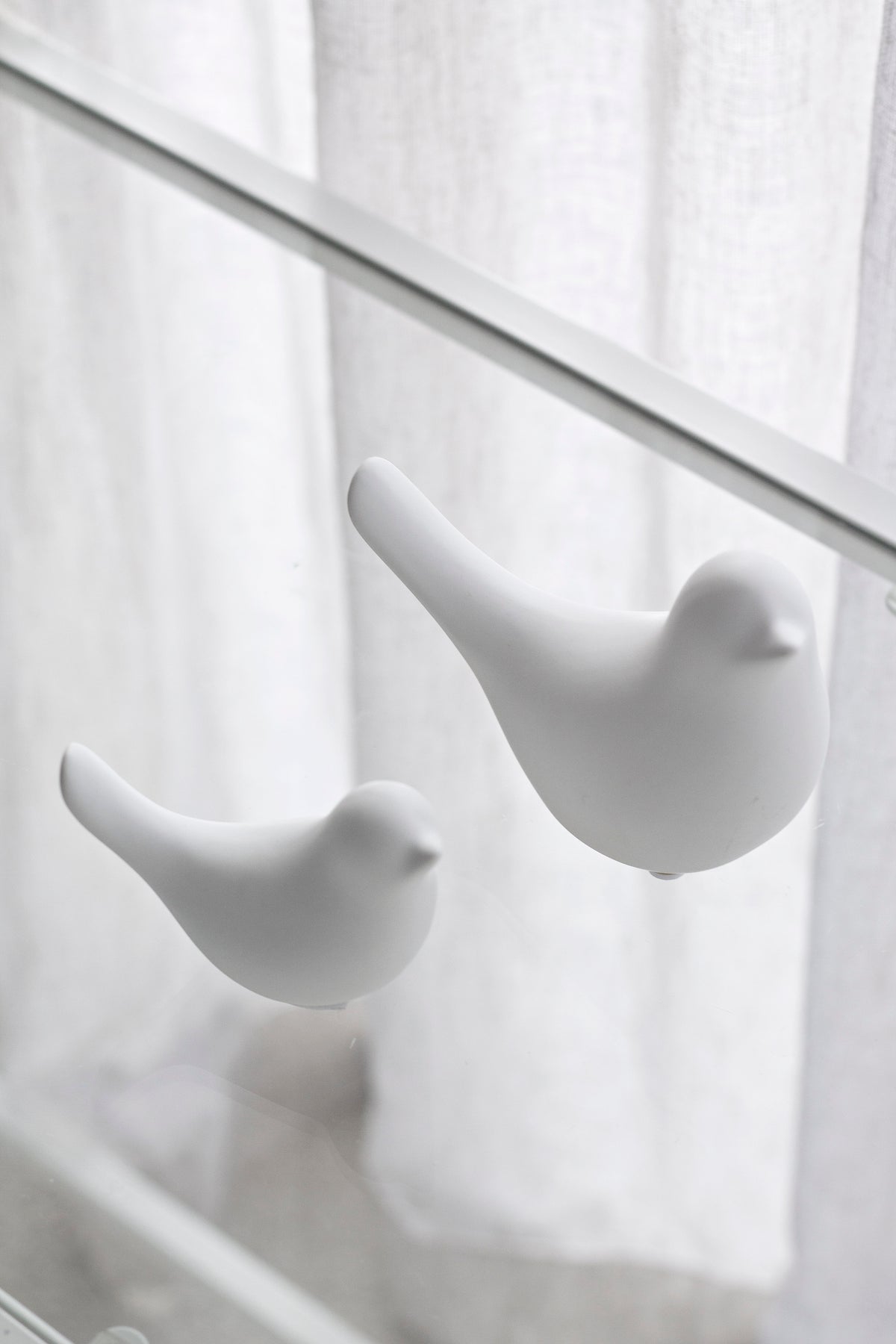 White Della doves on a glass shelf in front of sheer curtains