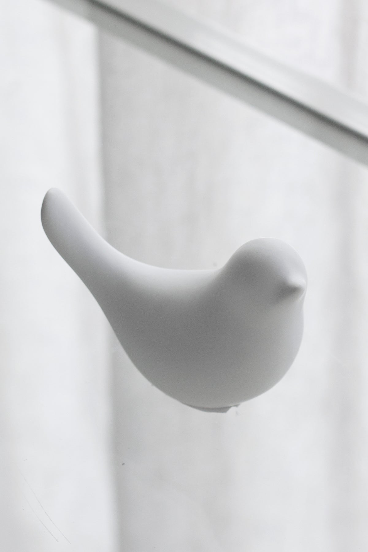 Single white Della ceramic dove against a sheer curtain, side view