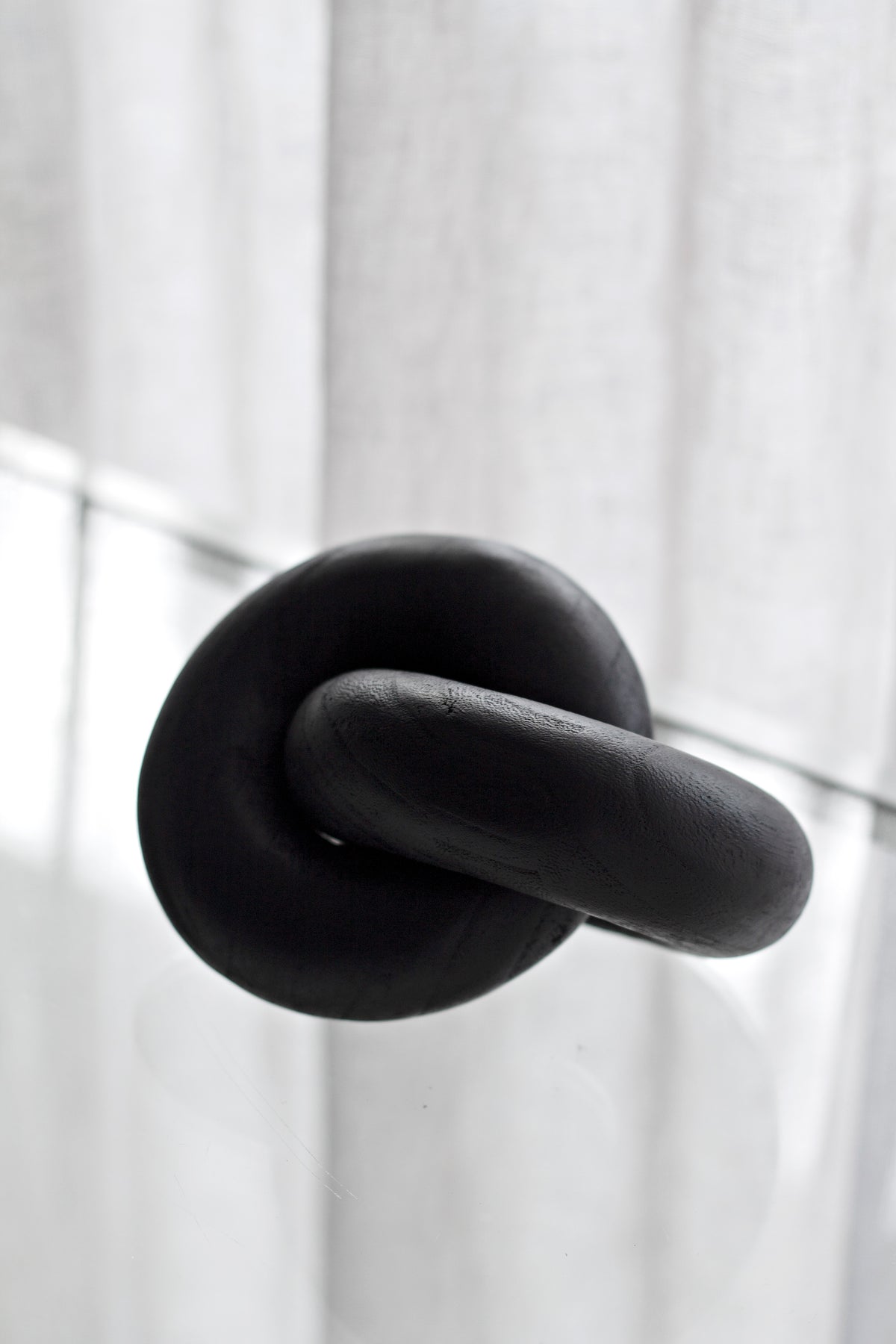 Black wooden knot sculpture on a white ledge, sheer curtain behind